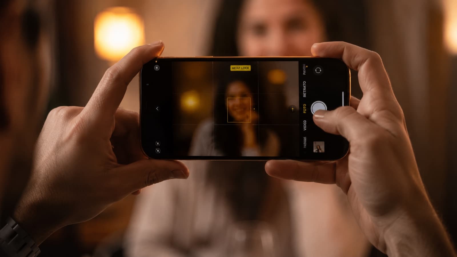 Manos sosteniendo el celular en horizontal con el indicador AE/AF LOCK y el recuadro de foco fijado en un rostro