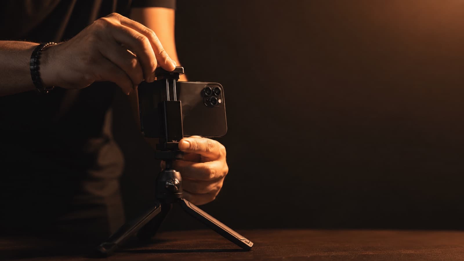 Close-up of hands clipping a phone into a tabletop tripod, warm light behind