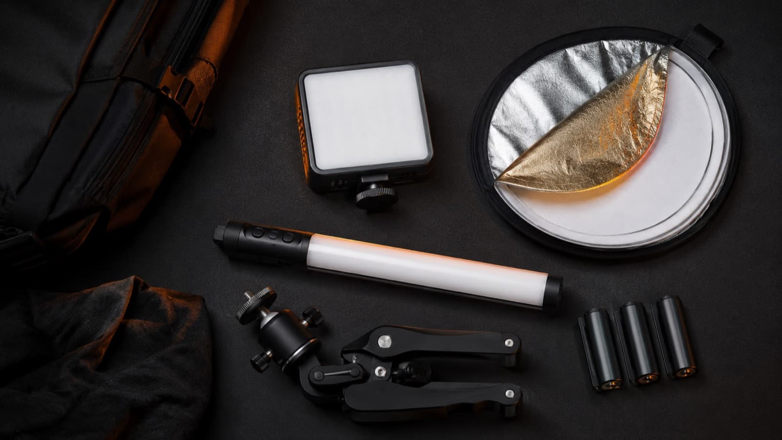 Flat-lay de un kit de luz ligero: panel pequeño, reflector plegado, tubo RGB, mini trípode y baterías