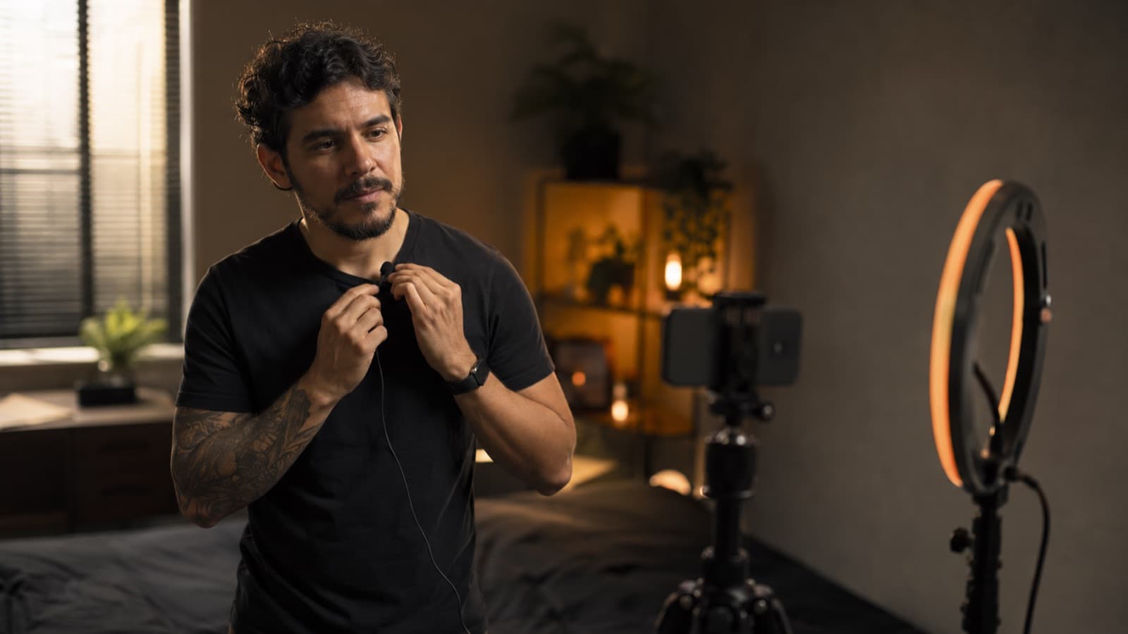 Un creador revisando el micrófono de solapa en un mini-set con ring light, antes de grabar