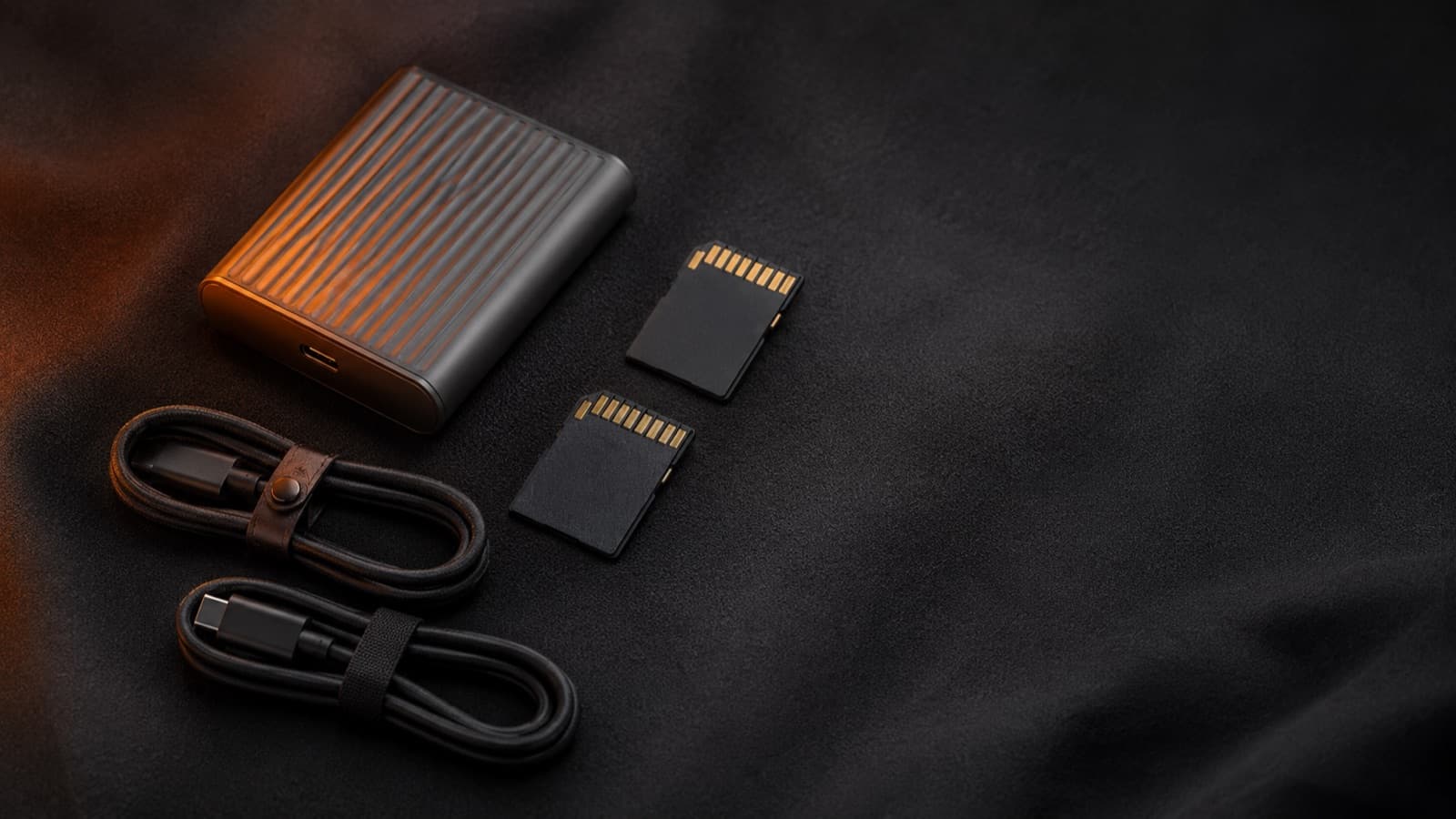 SD cards and a portable SSD with cables, in a flat-lay on a dark background
