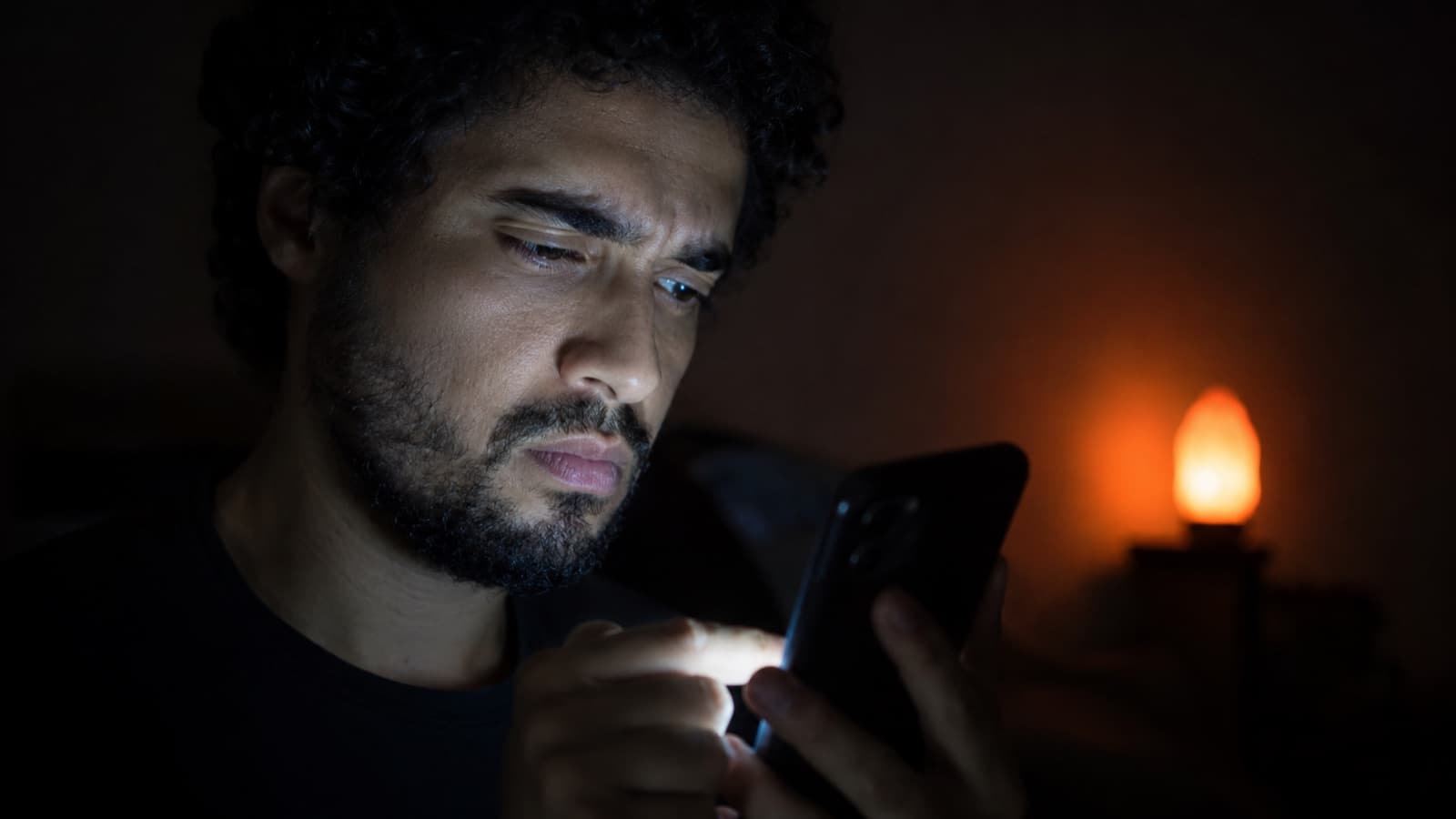 A person watching a phone with a critical, impatient expression, in the dark